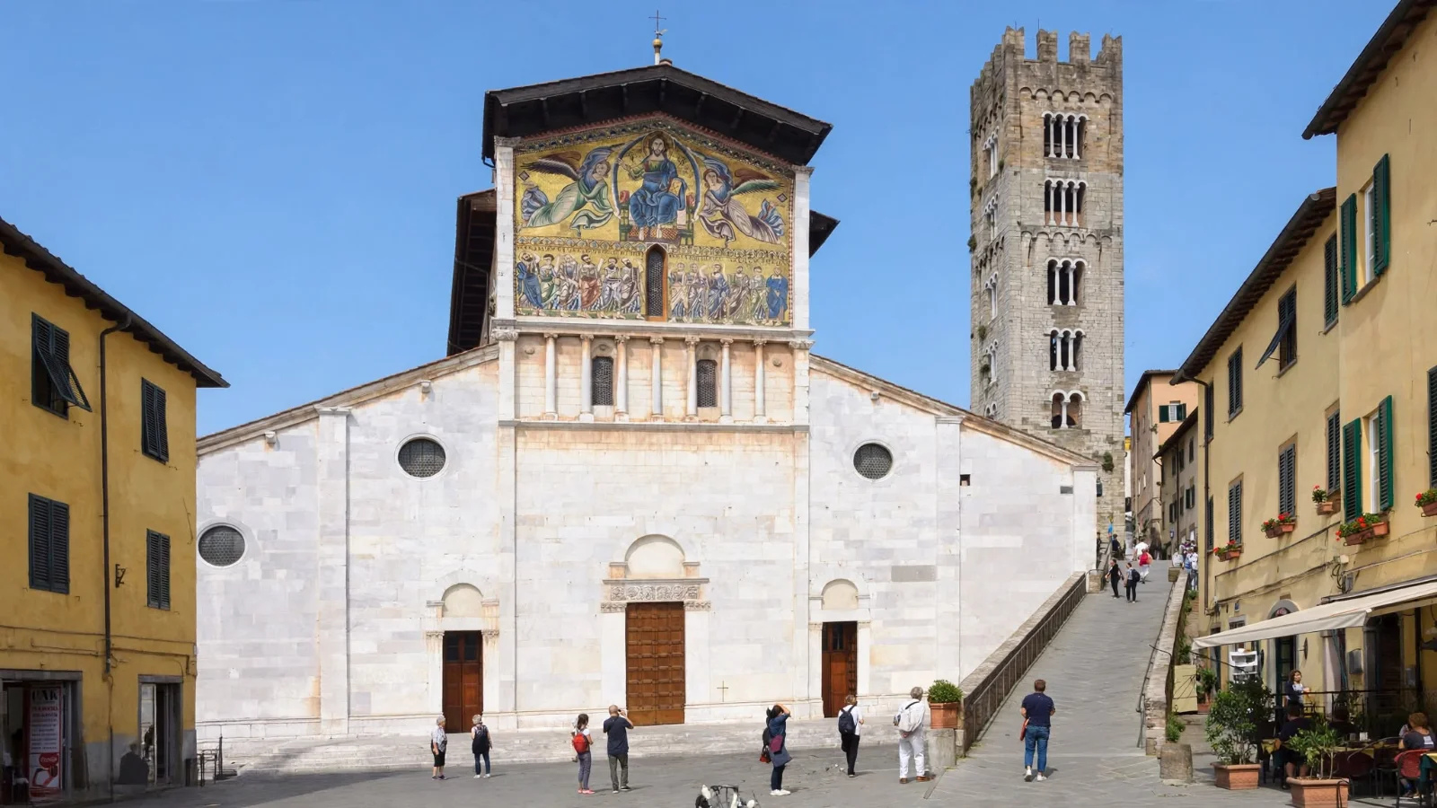 White marble facade of Basilica di San Frediano in Lucca featuring its 13th-century golden mosaic, stone bell tower, and sloped ramp area on the right side