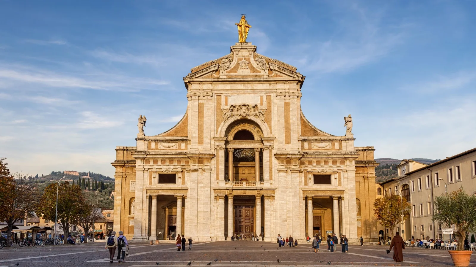 Basilica of Santa Maria degli Angeli in Assisi, a large baroque church with a golden statue of Mary on top, facing a flat paved square in the valley below the old town