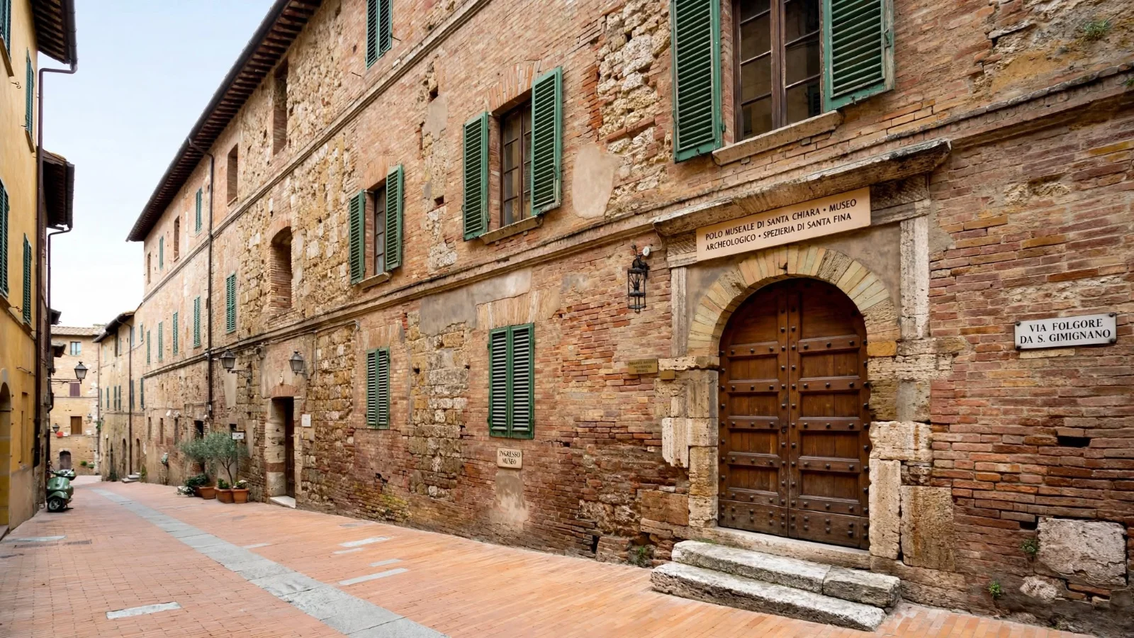 Exterior brick and stone facade of the Santa Chiara museum complex on Via Folgore da San Gimignano with two stone steps at the arched entrance