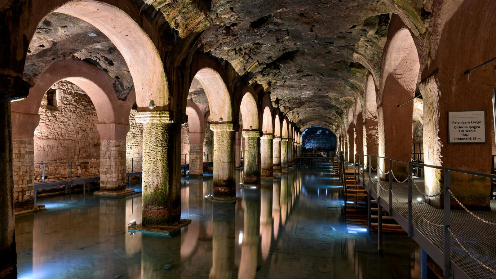 Illuminated underground caverns and stepped metal walkways inside the Palombaro Lungo water cistern in Matera