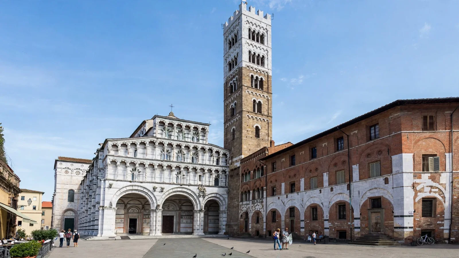 Facade of Duomo di San Martino in Lucca with three large ground-floor arches, tiered Romanesque marble colonnades, and the tall crenellated bell tower on Piazza San Martino