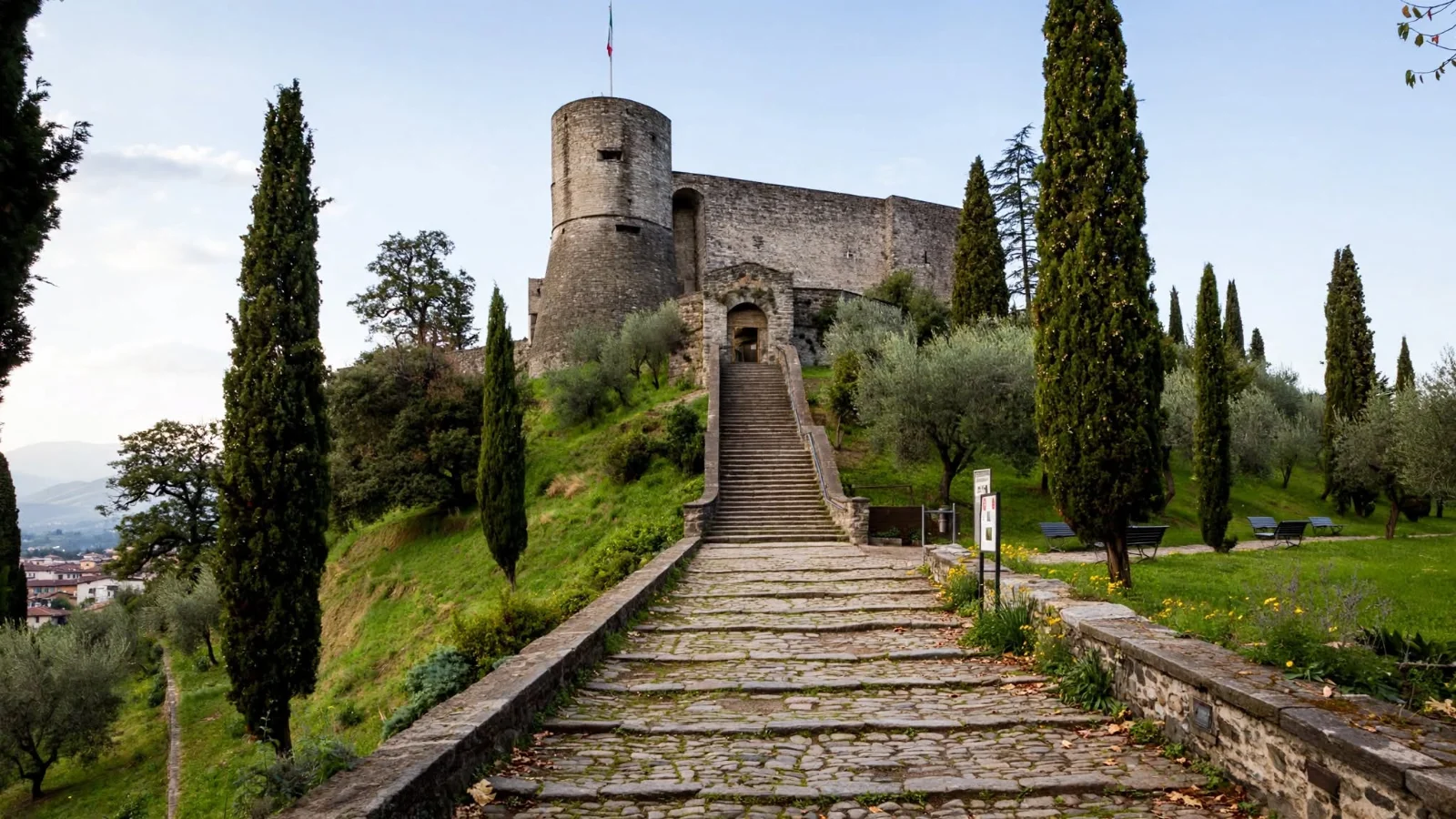 Medieval stone keep of the Rocca di Bergamo fortress surrounded by cypress trees on Eupilio hill, with stone steps at the entrance gate