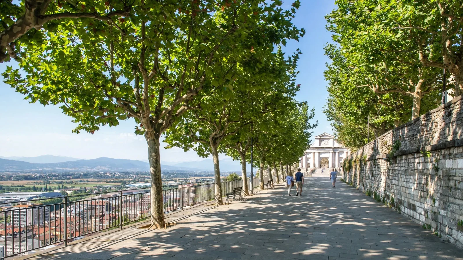 Tree-lined promenade along the Venetian Walls of Bergamo Città Alta overlooking the lower town, with the white marble Porta San Giacomo gateway in the distance