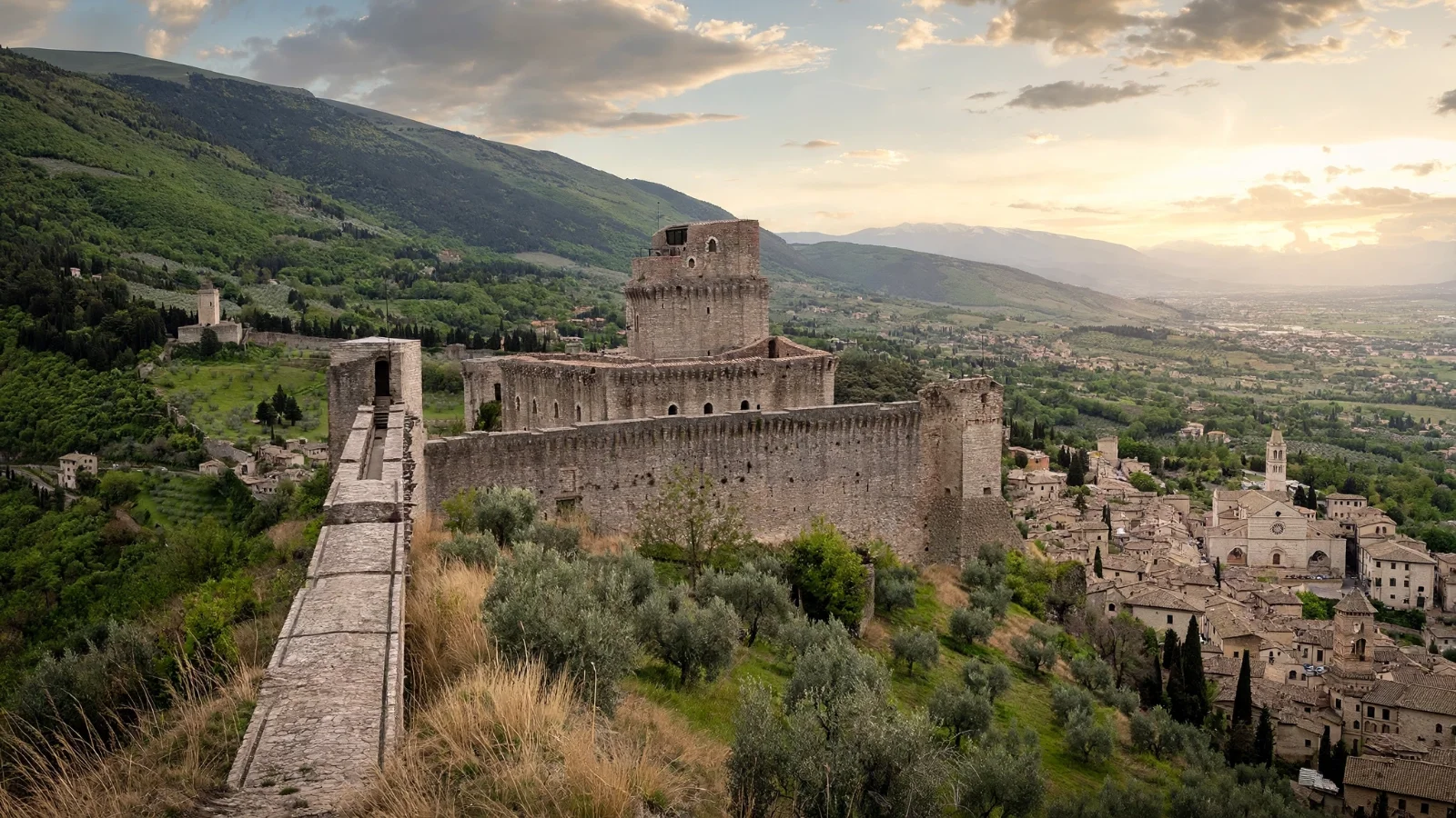 Rocca Maggiore, the medieval hilltop fortress of Assisi, with long stone walls and a square keep above the rooftops of the old town and the Umbrian valley