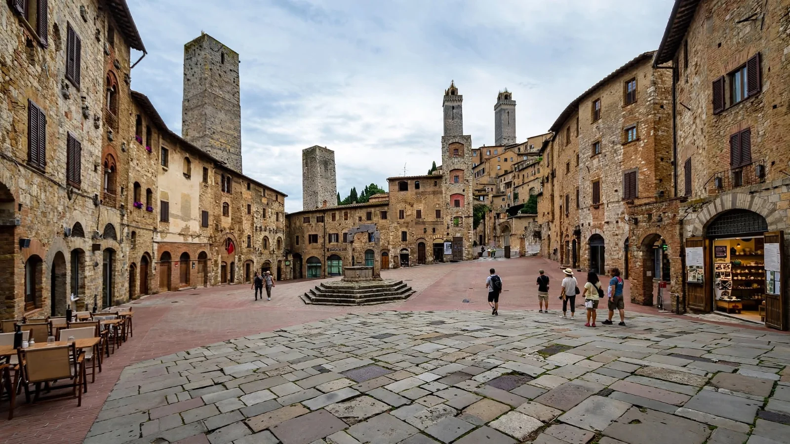 Brick-paved Piazza della Cisterna in San Gimignano with its octagonal medieval well, sloped triangular layout, and surrounding towers